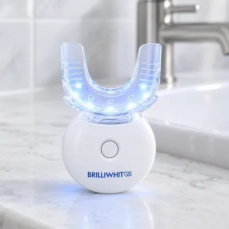 The BrilliWhite LED mouthpiece lit up, standing on a marble counter beside the tap