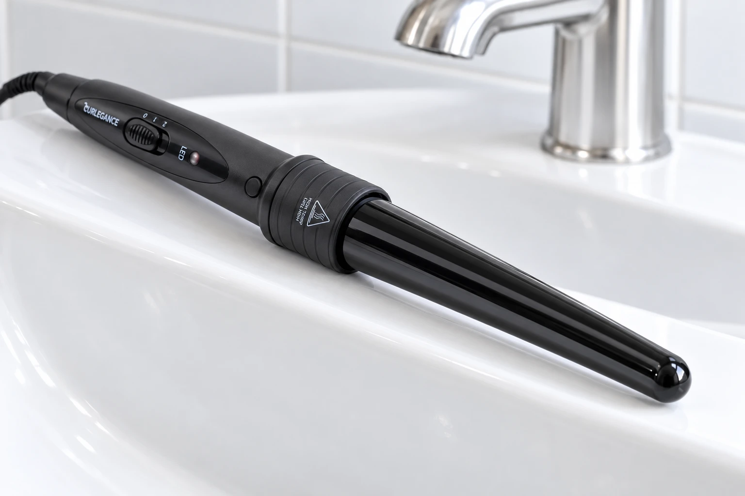 The Curlegance wand lying along the rim of a white basin, its tapered barrel and ribbed collar seen close