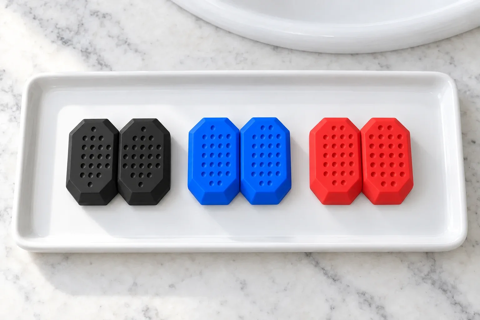 The three pairs of JawCore bite pieces, black, grey and white, on a white tray seen from above